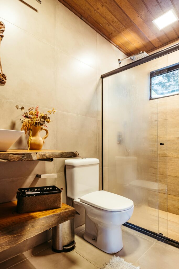 Warm bathroom with toilet, glass shower, wooden ceiling and rustic shelf.